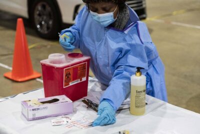 A nurse in blue PPE preparing vaccines.